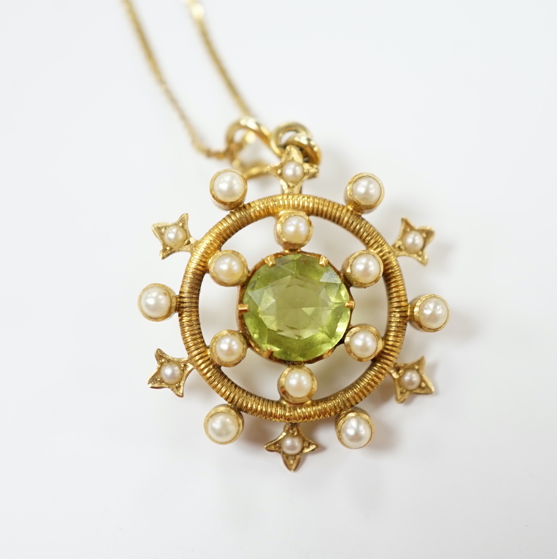 An Edwardian yellow metal, peridot and seed pearl cluster set 'wheel' pendant, overall 30mm, on a later 14k chain, gross weight 5.2 grams.